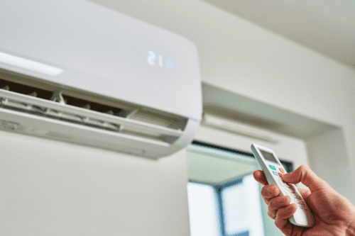 Pessoa ajustando a temperatura de um ar condicionado com controle remoto na parede, detalhes visíveis em uma sala moderna.