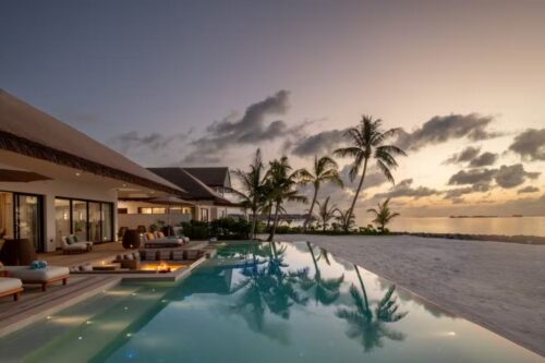 Vista luxuosa de uma vila à beira-mar no Hilton Maldives Amingiri Resort ao entardecer.
