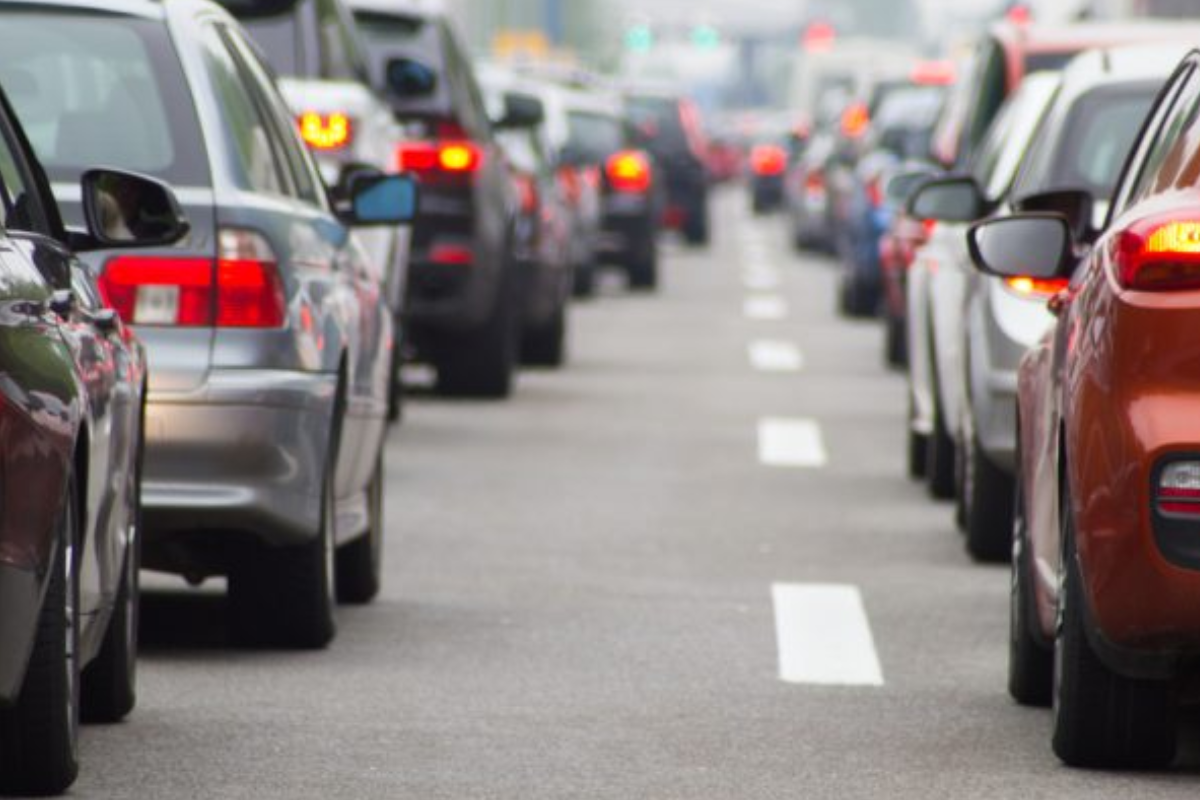 Vista traseira de diversos veículos parados em um congestionamento de trânsito em uma via urbana durante o dia.
