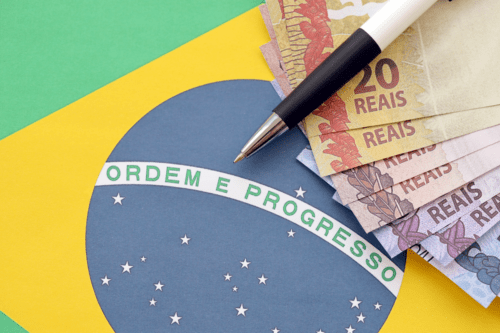 Dinheiro brasileiro em cédulas de 20 reais, uma caneta e uma bandeira do Brasil, com foco na promoção do progresso, ordem e progresso.