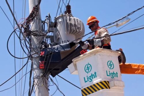 Fotografia em ângulo baixo de um eletricista da concessionária Light trabalhando em um poste de energia.