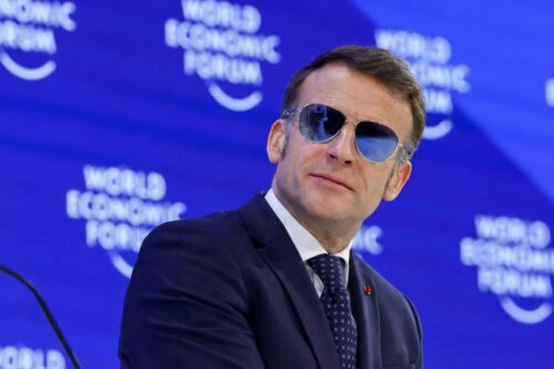 Retrato de meio corpo de Emmanuel Macron vestindo terno azul-marinho, camisa branca e gravata com pequenos padrões.