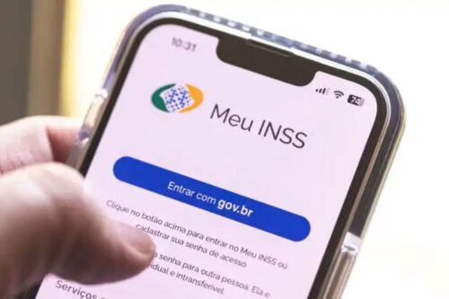Close-up de uma mão segurando um smartphone que exibe a tela inicial do aplicativo "Meu INSS".