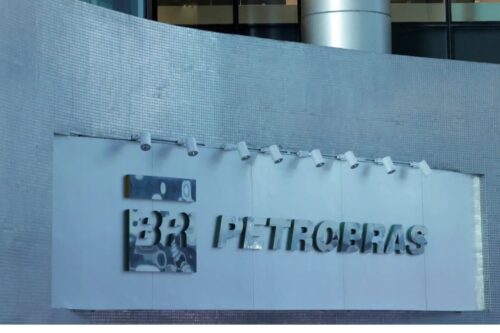 Fachada de um edifício com o logotipo da Petrobras em letras metálicas prateadas sobre uma placa branca, iluminado por pequenos refletores.