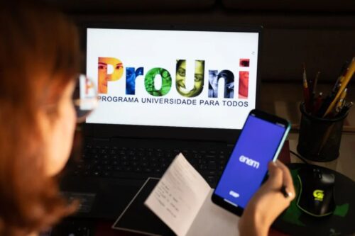 Uma pessoa vista de costas, levemente fora de foco, observa a tela de um notebook que exibe o logotipo colorido do "ProUni - Programa Universidade para Todos".