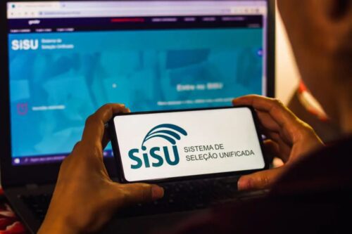 Pessoa segurando um smartphone que exibe o logotipo do SISU (Sistema de Seleção Unificada) em destaque.