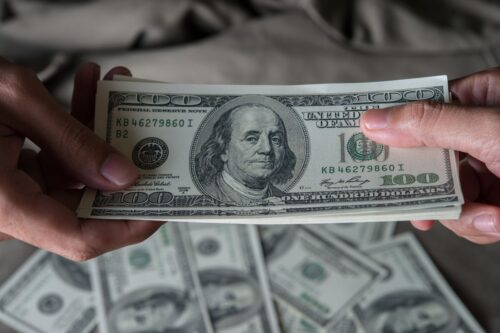 Close-up das mãos de duas pessoas segurando um maço de notas de 100 dólares americanos.