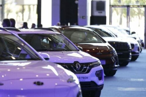 Fileira de carros modernos em exposição dentro de um showroom iluminado, com destaque para um veículo Renault branco em primeiro plano.