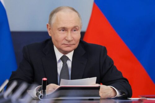 Fotografia em plano médio do presidente da Rússia, Vladimir Putin, sentado à mesa em um ambiente oficial.