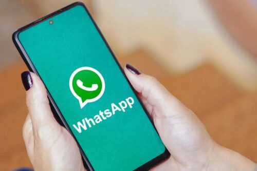 Mãos de uma pessoa segurando um smartphone que exibe o logotipo e o nome do aplicativo WhatsApp em uma tela verde.