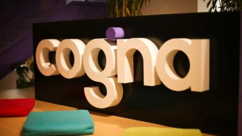 Logo da COGNA em ambiente corporativo; COGN (COGN3) representa a empresa do setor educacional no mercado financeiro.