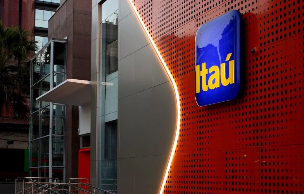 Fachada de agência do Itaú com logotipo iluminado em prédio moderno, vista externa em área urbana.