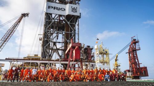 Equipe em plataforma offshore da Prio (PRIO3) reunida em frente à torre de perfuração, simbolizando operações de petróleo no Brasil.