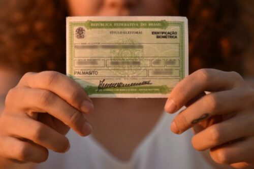 Pessoa segura título de eleitor 2026 nas mãos, documento eleitoral brasileiro usado para votar nas próximas eleições.