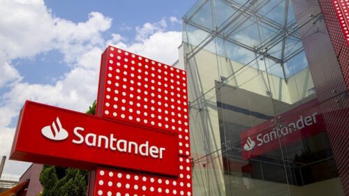 Fachada de agência do Santander com logotipo vermelho em destaque e prédio envidraçado ao fundo.