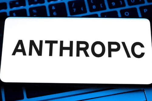 Smartphone exibindo o logotipo da empresa de inteligência artificial "ANTHROP\C" em letras pretas sobre um fundo branco. O aparelho está posicionado sobre o teclado retroiluminado em azul de um notebook.