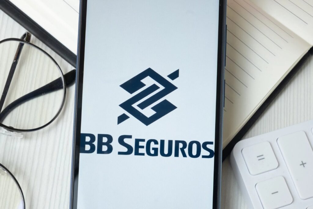 Logotipo da BB Seguros exibido na tela de um smartphone sobre uma mesa de escritório.