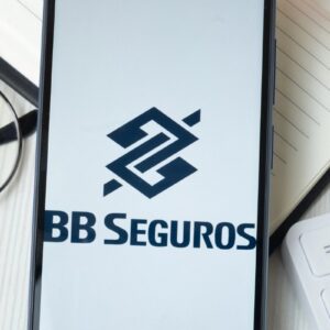 Logotipo da BB Seguros exibido na tela de um smartphone sobre uma mesa de escritório.