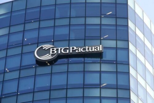 Fachada de um edifício moderno com vidros espelhados azuis, exibindo o logotipo e o nome do banco "BTG Pactual" em letras prateadas sobre uma estrutura metálica escura.