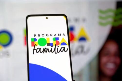 Primeiro plano de um smartphone exibindo o logotipo colorido do 'Programa Bolsa Família'.