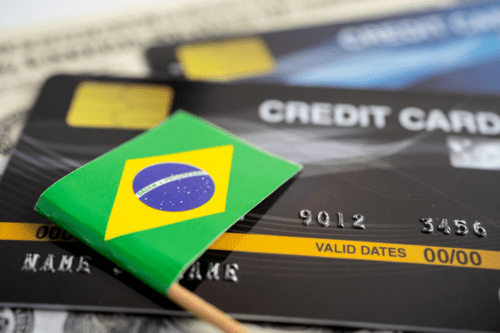 Cartão de crédito e uma bandeira do Brasil sobrepostos, representando transações financeiras no Brasil.