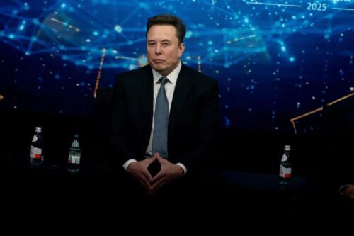 Fotografia de Elon Musk sentado em um palco durante um evento.