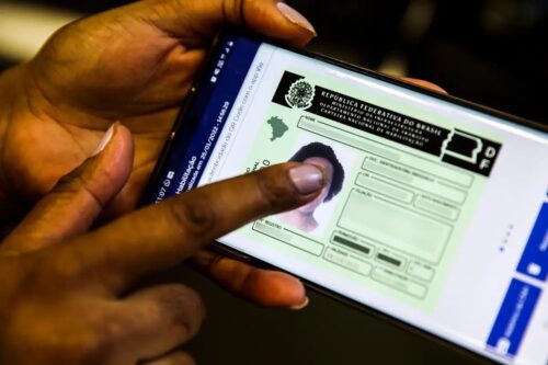 Close-up das mãos de uma pessoa segurando um smartphone que exibe a Carteira Nacional de Habilitação (CNH) digital brasileira.