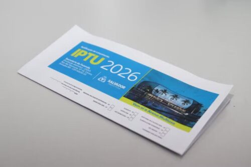 Foto em close de um carnê de pagamento do IPTU 2026 da Prefeitura de Salvador, sobre uma mesa cinza.