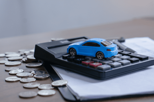 Imagem de uma calculadora ao lado de moedas, com um carrinho de brinquedo azul sobre a calculadora, simbolizando planejamento financeiro e compra de carro.