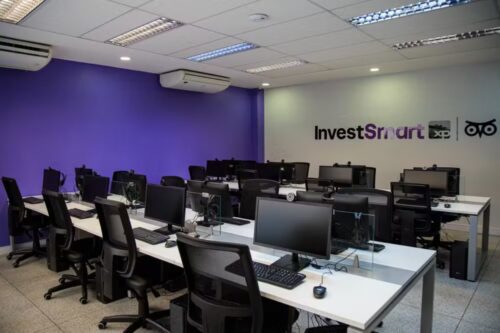 Escritório moderno da InvestSmart XP na Unisuam, com várias estações de trabalho alinhadas.