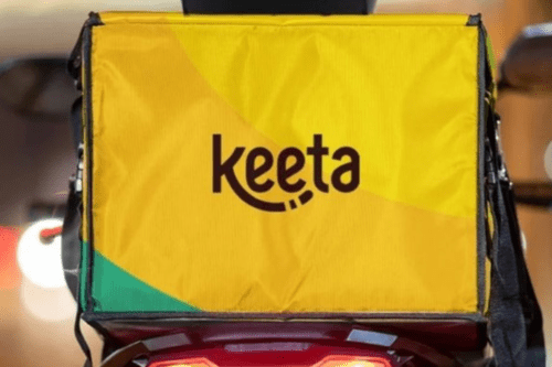 Mochila de transporte de alimentos da KeeTa acoplada a uma moto. O logotipo preto da marca aparece centralizado sobre o fundo amarelo vibrante, sugerindo serviço de delivery em operação.