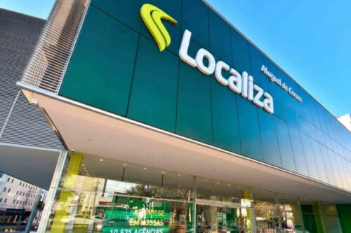 Fachada moderna de uma agência da Localiza em ângulo contra-picado. O destaque é o painel verde escuro com o logotipo da empresa em amarelo e branco.
