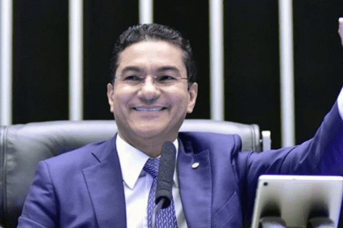 O político Marcos Pereira sorrindo, vestindo terno azul e gravata, sentado à mesa do Plenário da Câmara dos Deputados com um microfone à frente.