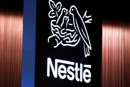 Logotipo da Nestlé iluminado em branco contra um fundo preto.