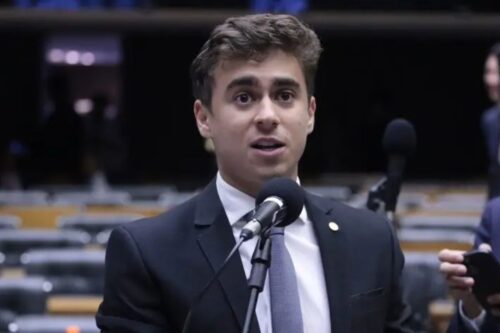 Fotografia do deputado Nikolas Ferreira em primeiro plano, falando ao microfone em uma tribuna parlamentar.