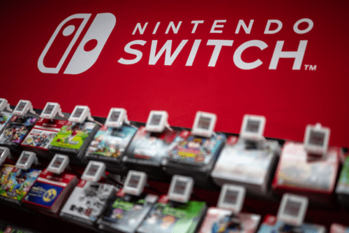 Prateleira de loja exibindo diversos jogos de Nintendo Switch em destaque. Ao fundo, um painel vermelho vibrante exibe o logotipo branco da "Nintendo Switch".