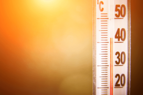 Termômetro de vidro com escala em Celsius mostrando aproximadamente 48 graus, fundo desfocado com cores quentes, ideal para imagens relacionadas a clima quente.