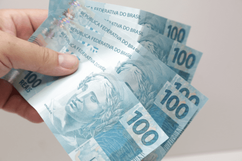 Mão segurando cédulas de 100 reais do Brasil.