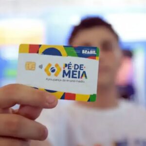 Close-up de uma mão segurando o cartão do programa "Pé-de-Meia", do Governo Federal do Brasil.