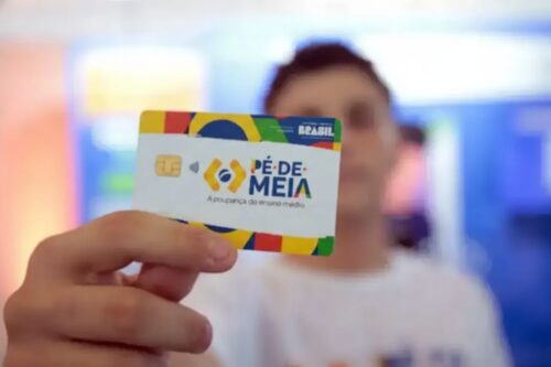 Close-up de uma mão segurando o cartão do programa "Pé-de-Meia", do Governo Federal do Brasil.