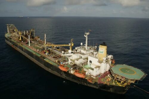 Vista aérea de uma plataforma de petróleo da Petrobras navegando em mar aberto sob um céu com poucas nuvens, exibindo a estrutura de perfuração e o heliponto.