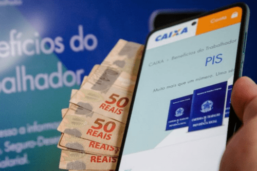 Mão segurando um smartphone que exibe o aplicativo da Caixa Econômica Federal com a palavra 'PIS' em destaque. Ao fundo, notas de 50 reais e um cartaz azul com a frase 'Benefícios do Trabalhador'.