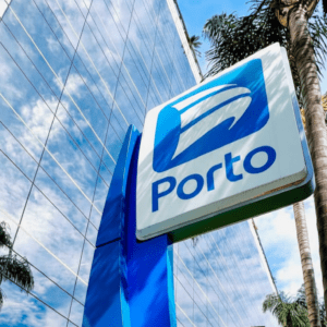 Fachada de um edifício comercial moderno com vidros espelhados, destacando em primeiro plano uma placa vertical azul e branca com o logotipo e o nome "Porto".