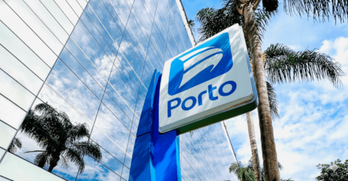 Fachada de um edifício comercial moderno com vidros espelhados, destacando em primeiro plano uma placa vertical azul e branca com o logotipo e o nome "Porto".