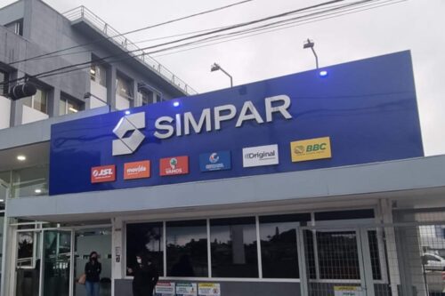 Fachada de um prédio da holding Simpar, com um grande painel azul exibindo o nome da marca e os logotipos de suas subsidiárias, como JSL, Movida, Vamos e Banco ABC.