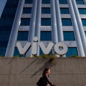 Uma mulher caminha pela calçada em frente à fachada moderna de um edifício corporativo da Telefônica Brasil. No