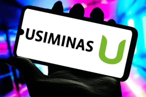 A imagem apresenta um smartphone segurado por uma mão em silhueta, centralizado contra um fundo vibrante e desfocado com luzes neon em tons de rosa, azul e roxo. A tela do aparelho, em um fundo branco brilhante, exibe em destaque o logotipo da Usiminas