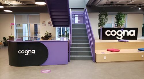 Interior da sede da Cogna Educação, com logo da empresa em destaque em ambiente corporativo moderno.