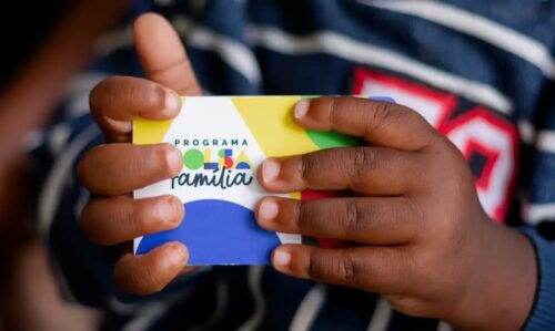 Criança segura cartão do programa Bolsa Família com as duas mãos, em destaque.