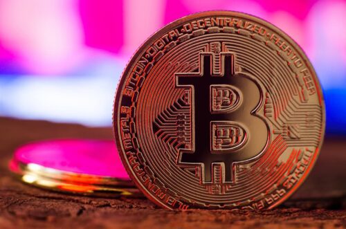 Moeda de Bitcoin em destaque com fundo colorido, representando queda e volatilidade no mercado cripto.